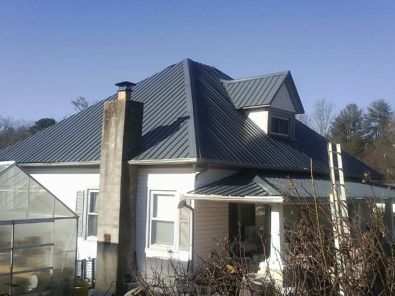 Dark blue standing seam metal roof on a white farmhouse with dormer — Slate & Tile Roof Repair by Roofing Brothers in Kimbolton
