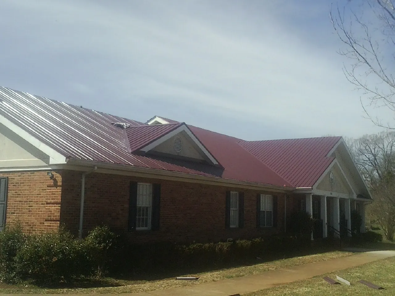 Red metal roof with gabled entries on a long brick building, from a Hail Damage Roof Repair job in Kimbolton