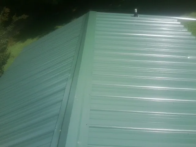 New green metal panels meeting at the ridge of a roof — Flat Roof Repair work by our crew in Kimbolton