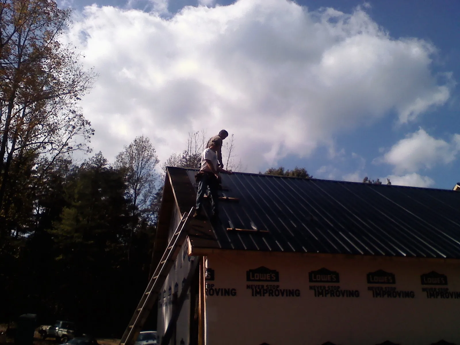 Roofer fastening dark metal panels high against a cloudy sky, from a Roof Inspection job in Kimbolton