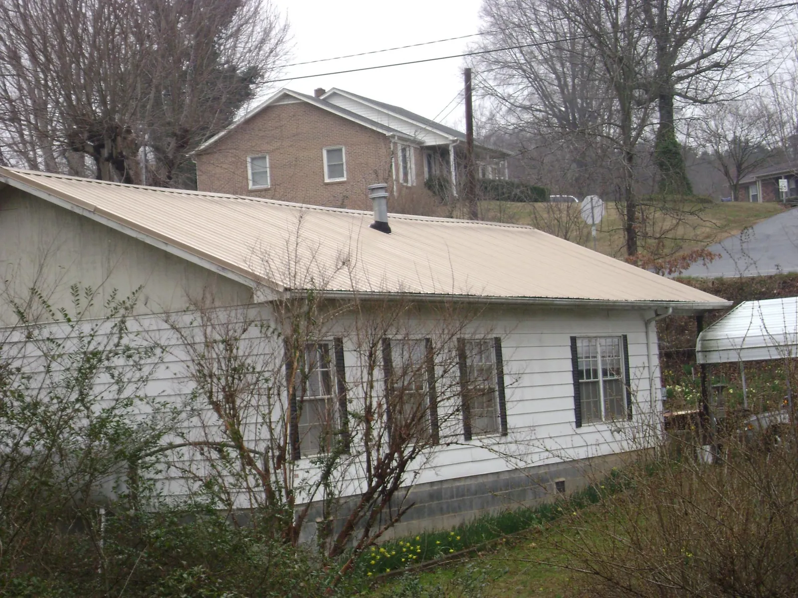 Tan metal roof on a white sided house set into a hillside — Commercial Roofing by Roofing Brothers in Kimbolton