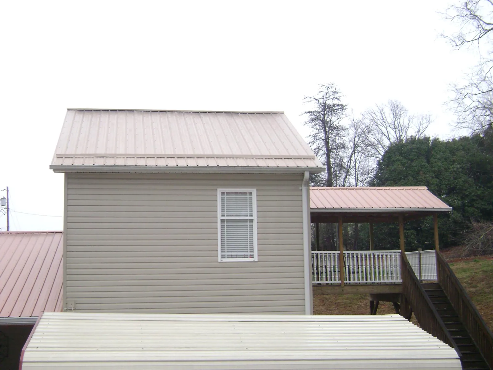 Tan metal roofs on a two story addition and attached porch, from a Roof Replacement job in Kimbolton